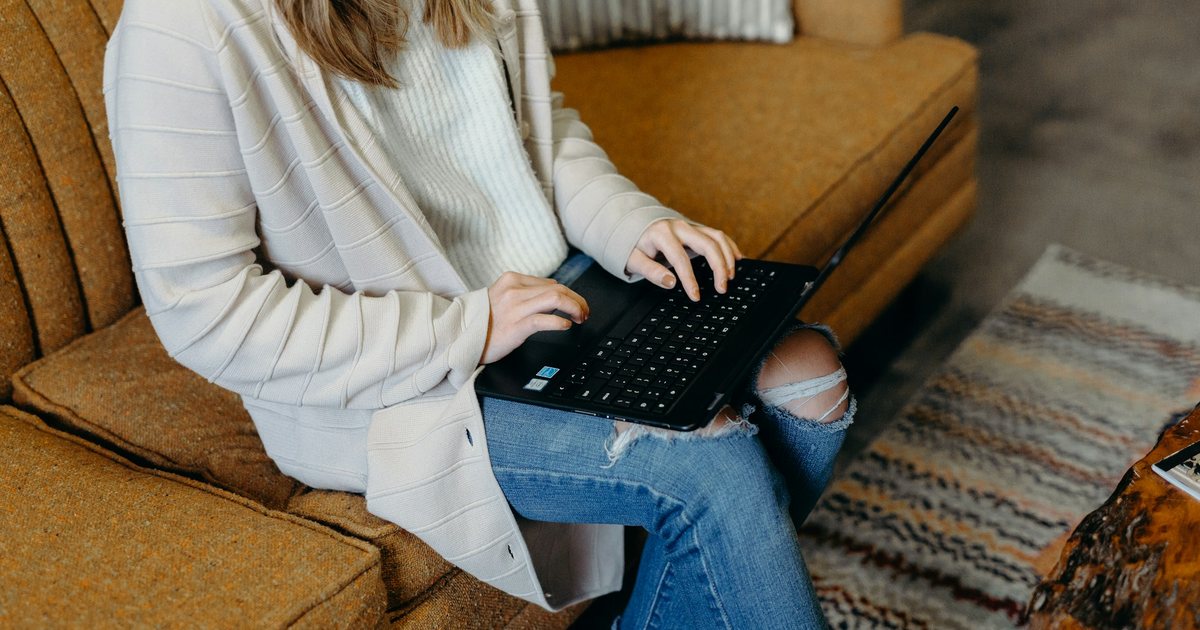 A person typing on a laptop on a sofa